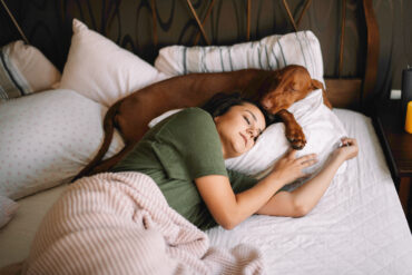 Woman relaxing in bed with her dog, symbolizing calm mornings and mindful rest.