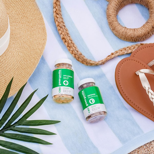  Vegan CBD herbal capsules on a beach towel with a sun hat, palm leaf, and flip flops.