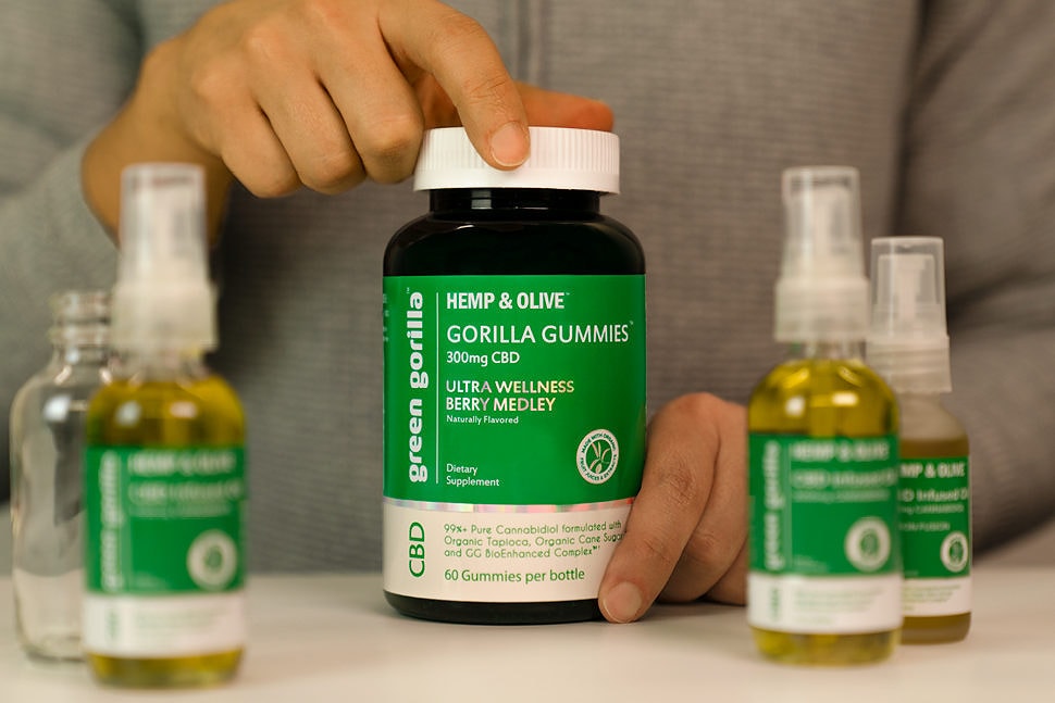 Person holding Green™ 300mg Berry Medley gummy bottle on table with four other CBD bottles