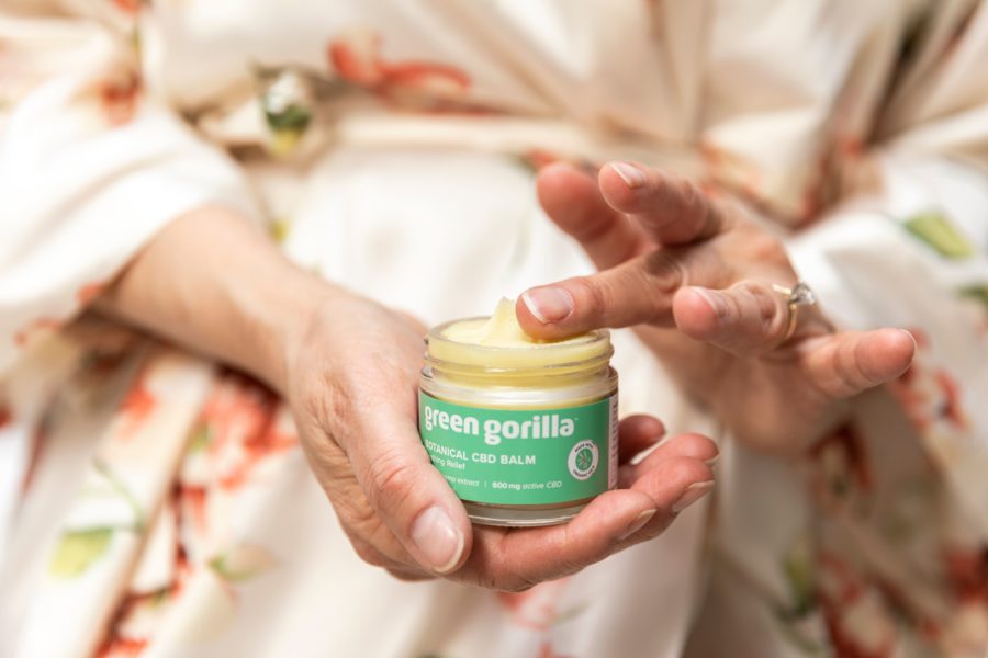 A woman in a robe holding a jar of CBD hemp balm