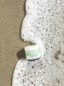 Jar of Green Gorilla™ CBD Face Crème lying on a sandy beach surrounded by white ocean foam