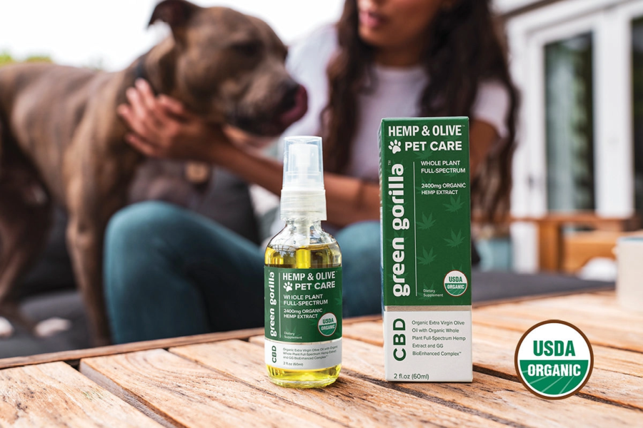 A dog and pet owner socializing in the background with a bottle of pet CBD oil for sale in the foreground.