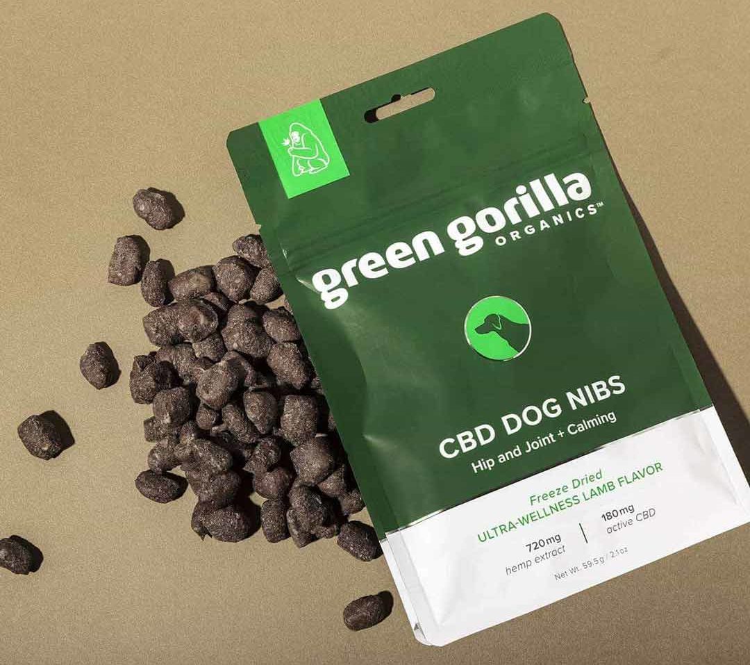 A dog and pet owner socializing in the background with a bottle of pet CBD oil for sale in the foreground.