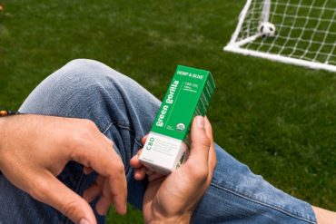 Person holding a box of Green Gorilla™ CBD oil on a soccer field