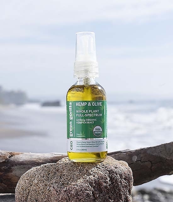 A bottle of Green Gorilla™ CBD oil on rock in front of a beach.