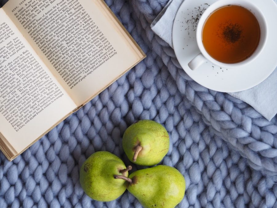 Three pears, an open book, and a cup of tea on a blue knitted blanket