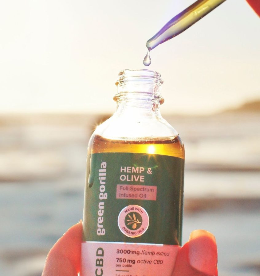 A person holding a bottle of 3000mg CBD hemp extract oil and a dropper with an ocean sunset in the background