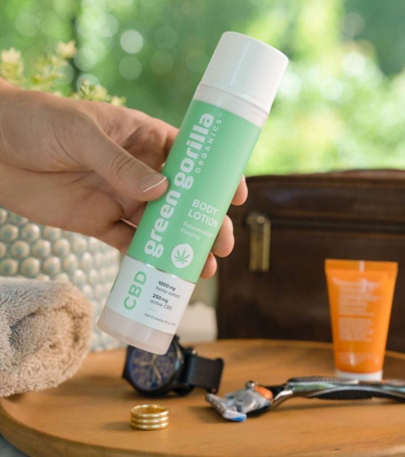 A hand holding CBD body lotion in front of a table with a razor and towel.
