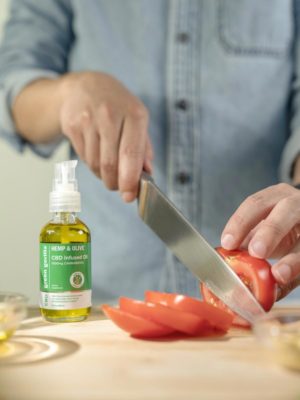 Someone slicing a tomato next to a bottle of CBD oil