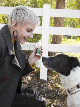 Light-haired woman holding a bottle of Green Gorilla™ CBD oil for pets in front of a black-and-white dog outside