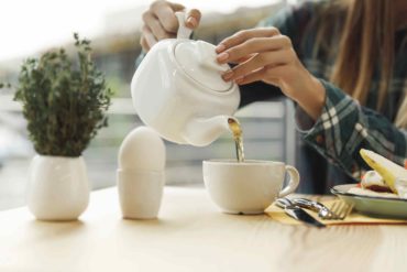 Woman pouring immune-boosting tea into a white teacup Filename: woman-pouring-tea