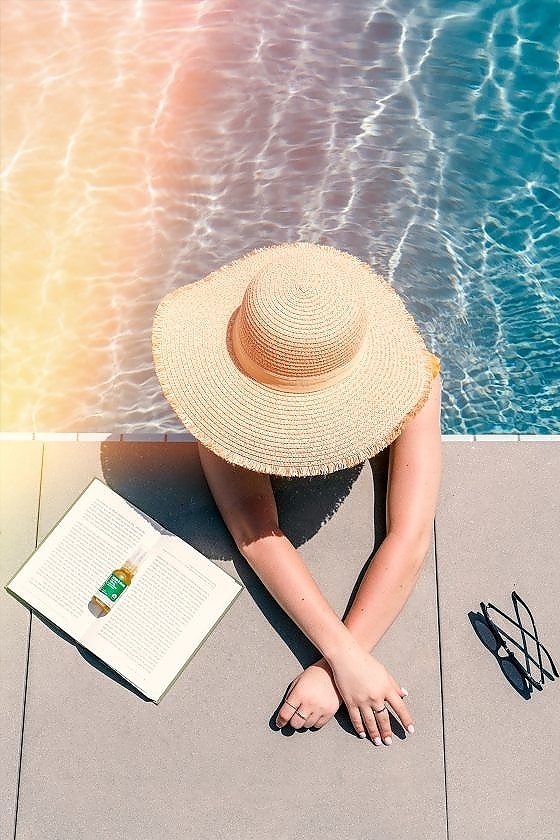 A woman in sunhat at the swimming pool enjoying a book and Green Gorilla™ lab-tested CBD oil.